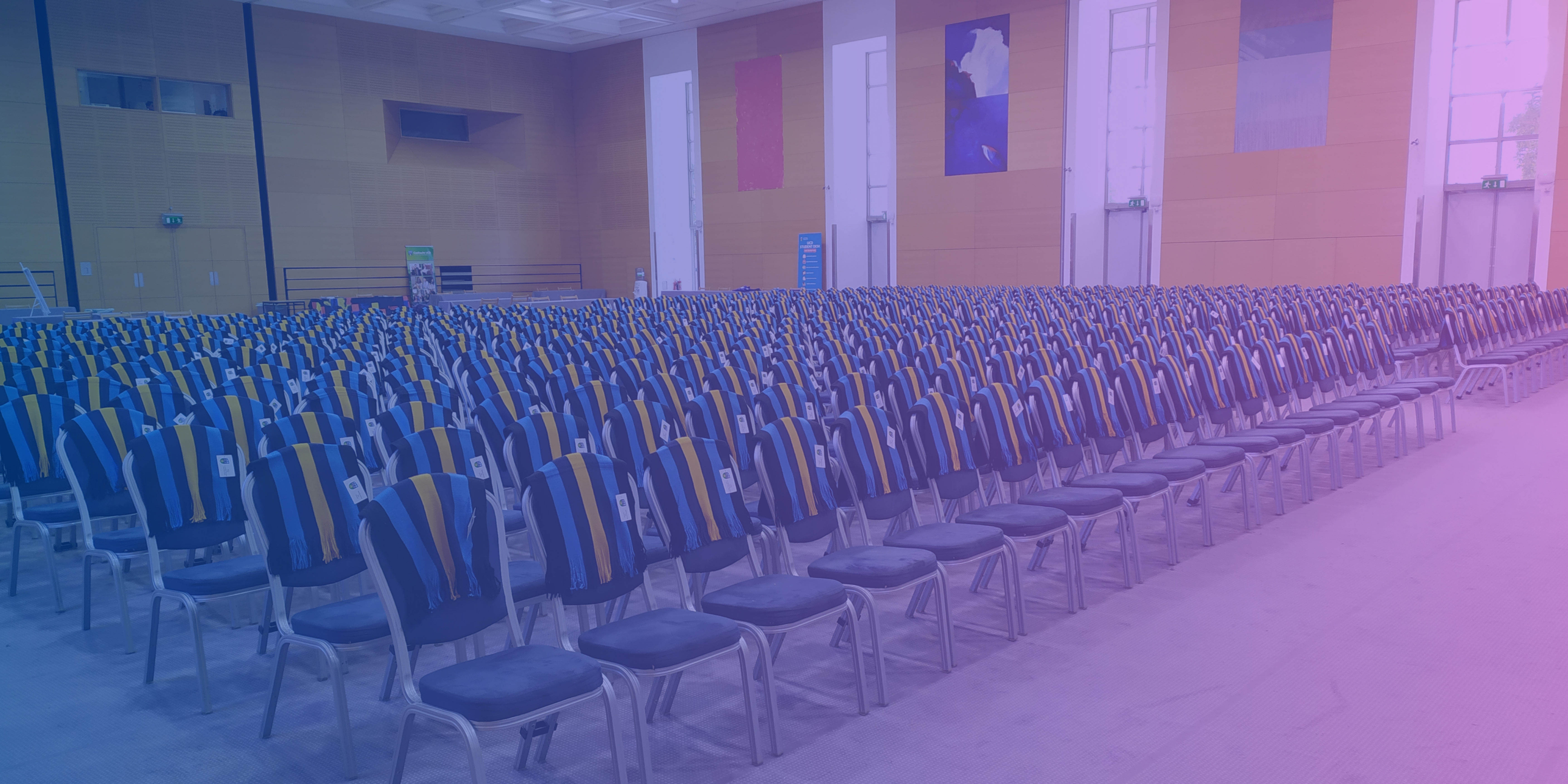 A large hall filled with chairs that have UCD scarves draped over their backs